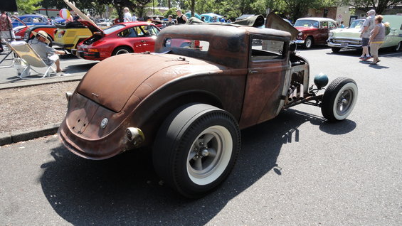 Rusty hot rod coupe with wide rear tires and exposed engine components, viewed from the rear