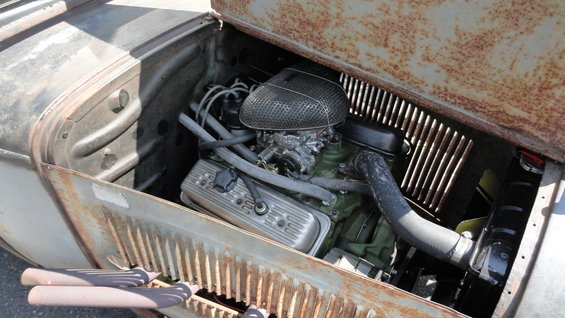 Engine bay of a rusty hot rod with a V8 engine and chrome valve covers