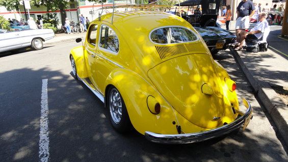 yellow Volkswagen Beetle parked on street, other cars and people visible