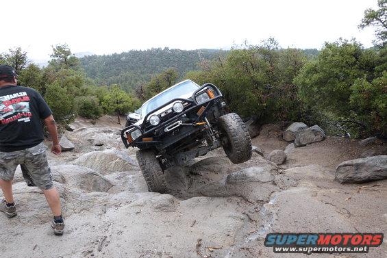 White off-road SUV climbing over rocks with a man watching