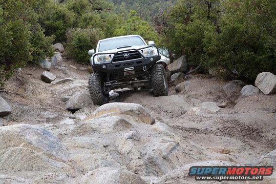 White Toyota pickup truck with aftermarket bumper navigating a rocky trail