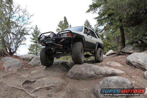 Two-tone white and black Toyota 4Runner with off-road modifications navigating a rocky trail