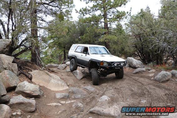 1985 Toyota 4Runner navigating a rocky off-road trail with trees and boulders