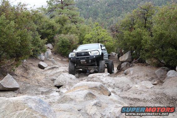 Toyota Tacoma with aftermarket bumper driving over rocks on a trail