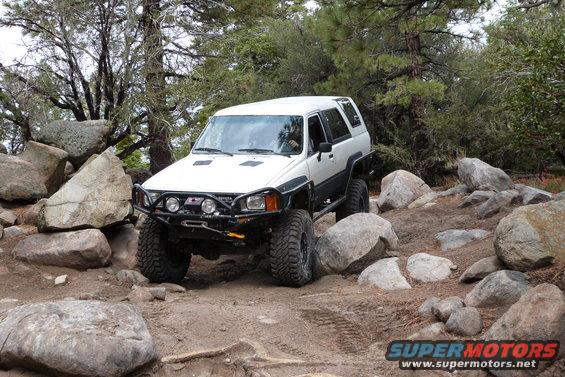 White Toyota 4Runner with aftermarket bumper and large tires navigating rocky terrain