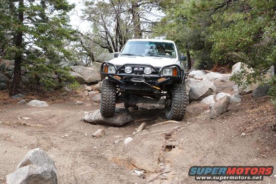 White Toyota 4Runner navigating a rocky trail, modified with a winch and off-road tires