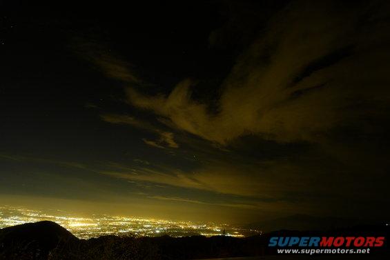 Night view of a city lights below dark clouds and stars