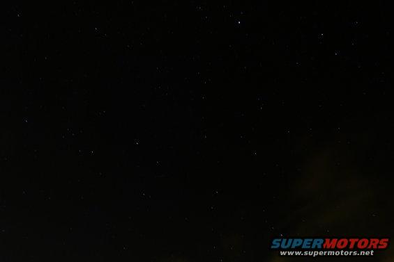 night sky full of stars, with a faint glow on the horizon and a website watermark