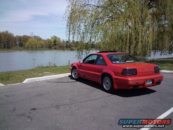 Red 1991 Pontiac Grand Prix coupe parked near a lake with a weeping willow tree overhead