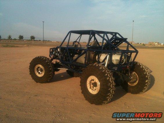 Custom blue off-road buggy with large tires and roll cage parked on dirt