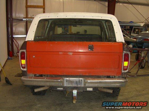 Rear view of a 1978 Ford Bronco with an orange tailgate and white removable top. It has a chrome bumper and dual exhaust pipes