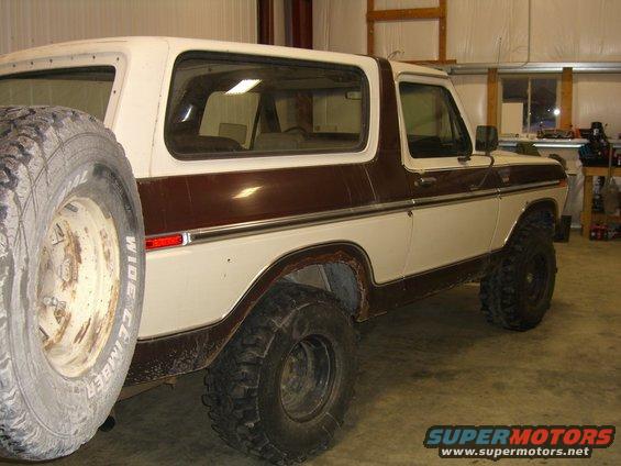 White and brown Ford Bronco with spare tire mounted on the back. It's in a garage
