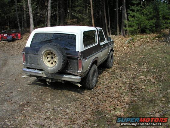 Ford Bronco parked on a dirt path in woods. Spare tire mounted on rear door