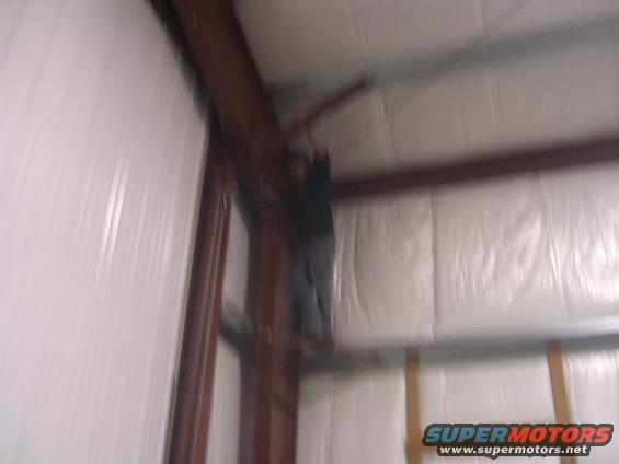 Person working on metal beams inside a building with white insulated walls. Supermotors.net logo visible