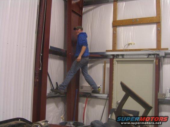 Guy in blue hoodie and jeans walking on metal beams inside a garage