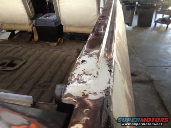 Interior of a vehicle with tan seats and a metal floor, showing rust and peeling paint on a body panel