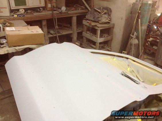 Car door prepped for paint in a workshop, with tools and supplies in background
