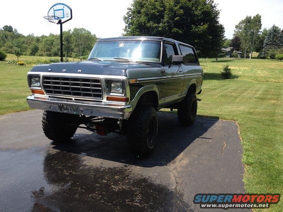 Dark green Ford Bronco with lifted suspension and large tires, parked on a wet driveway