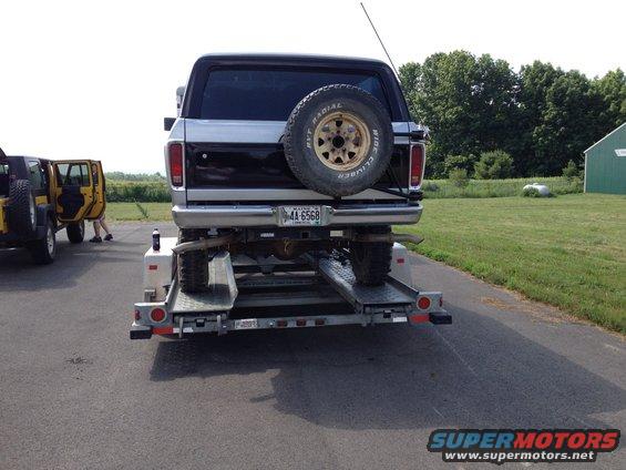 Rear view of a black and silver Ford Bronco on a trailer, with a yellow Jeep in the background