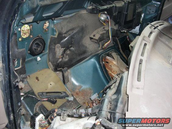 Interior of a vehicle with firewall removed, showing exposed wiring and components. Some rust is visible