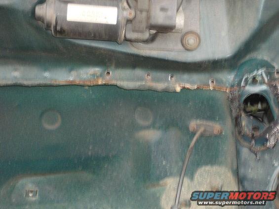 Green car firewall with motor and rusted edge. Holes drilled along the top edge