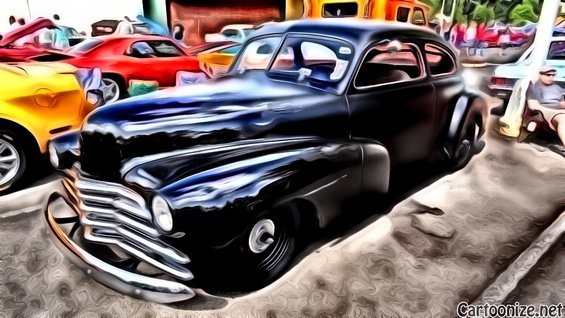Black coupe with chrome grille and fender details, parked outdoors with other cars