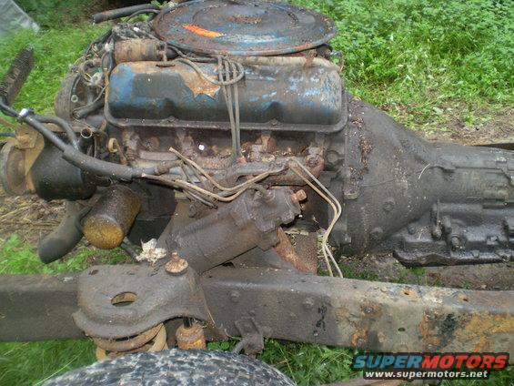 Engine and transmission assembly from an old vehicle, sitting on a frame with grass in the background