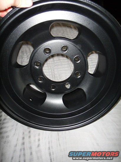 Black 5-spoke alloy wheel with a matte finish, held by a hand at the top