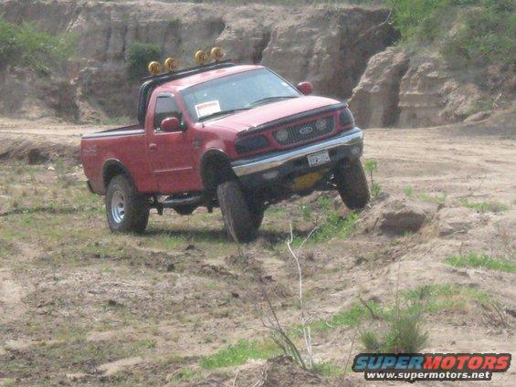 Red pickup truck with off-road tires driving on a dirt hill. It has a light bar on the roof