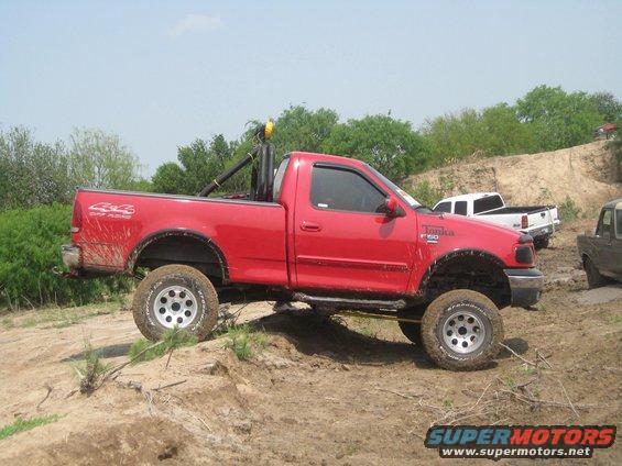 Red pickup truck with off-road tires and roll bar, side view