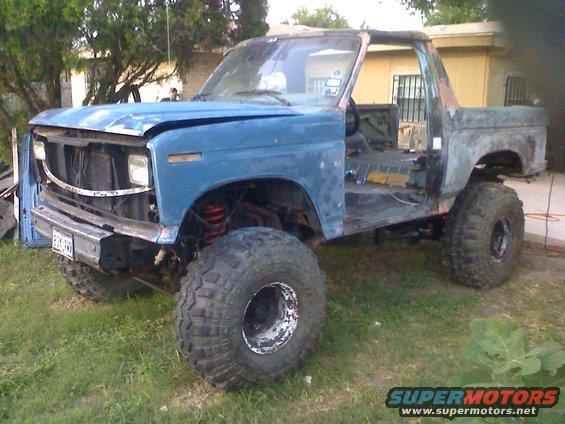 Blue Ford Bronco with lifted suspension and large tires, missing doors and hood