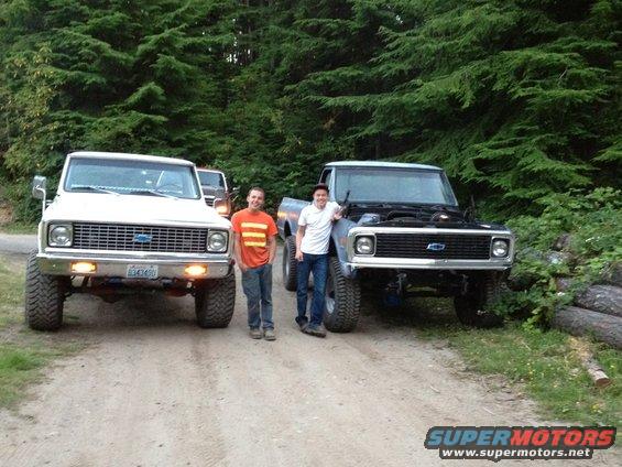 Two guys stand by lifted 1970s Chevy pickup trucks on a dirt road