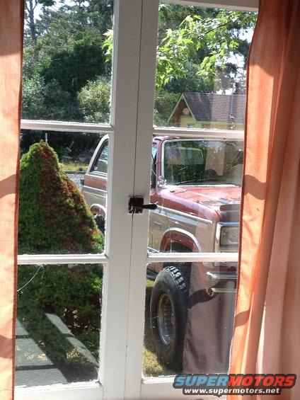 Red and tan Ford Bronco parked outside, seen through a window. Large tires are visible