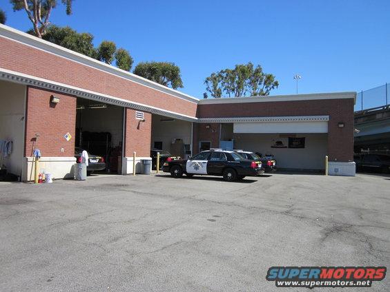Two police cars parked outside a brick building with open bays. One car has "HIGHWAY PATROL" on the side