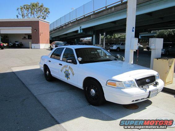 White 2003 Ford Crown Victoria police car with 'HIGHWAY PATROL' text, parked on pavement under an overpass