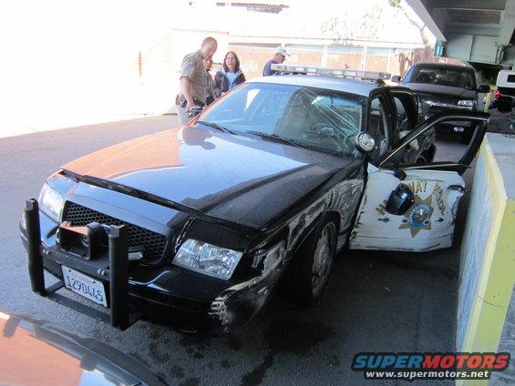Damaged police car with California Highway Patrol markings, front end smashed, driver door open. Another vehicle behind it