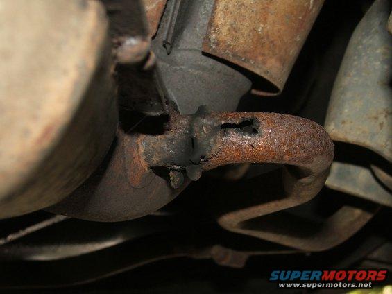 Rusted exhaust pipe with a hole, part of a vehicle's undercarriage