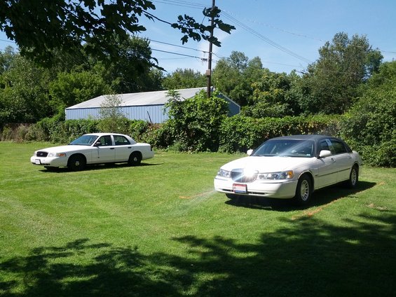 Two white sedans, one Ford Crown Victoria and one Lincoln Town Car, parked on a grassy lawn