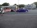 1970 Ford Ranchero - A purple customized coupe with pink racing stripes is seen driving on a street next to a bus.
