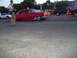 1970 Ford Ranchero - A man photographs a classic red sedan as it drives down the road, with other vehicles visible.