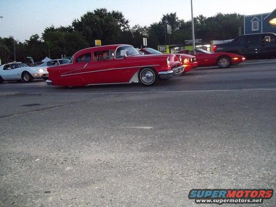 Red 1955 Chevrolet sedan with white trim and chrome wheels, seen from the side