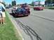 1970 Ford Ranchero - A custom black car with red accents drives down the road, with other vehicles and spectators present.