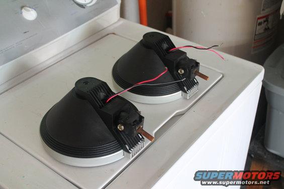 Two black automotive lighting components with wires and heat sinks sit on a white surface