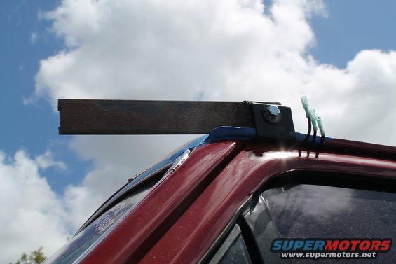 Close-up of a custom metal bracket attached to the roof of a red vehicle, with wires extending from it