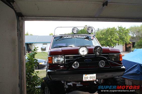 Front view of a lifted red Ford F-Series truck with extra lights and a 'Rough Country' sticker on the windshield