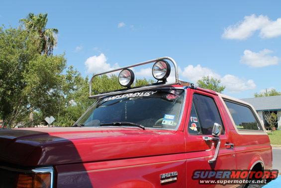 Red 1990 Ford Bronco with a chrome light bar and two large spotlights mounted on the roof