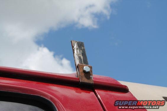 Custom metal light mount bolted to red vehicle roof edge