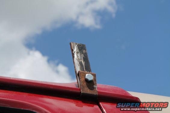Close-up of a rusty metal bracket bolted to the red roof of a vehicle