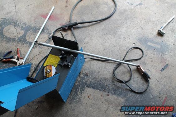 Blue welding machine with metal rods and clamps on concrete floor. A cut-off wheel is visible on the machine