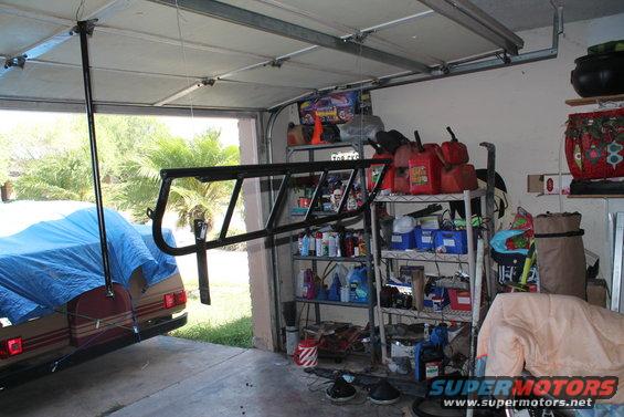 Roll cage hanging in garage, vehicle covered with blue tarp in background